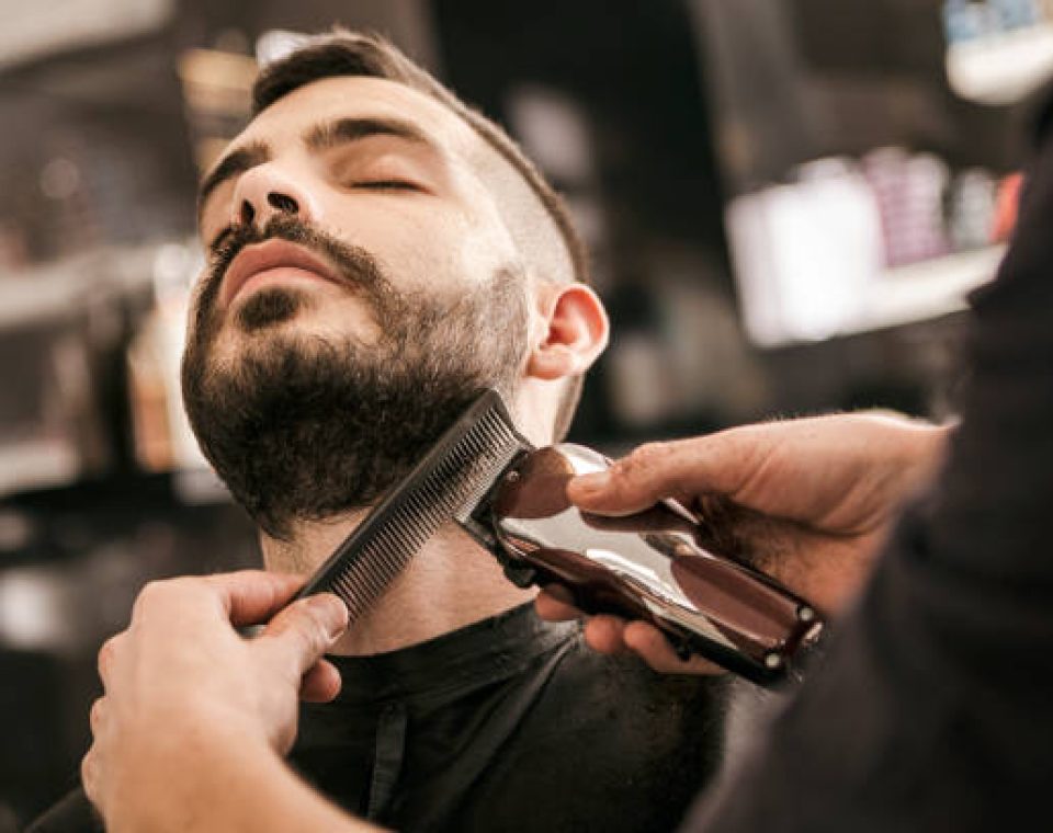 Man getting his beard trimmed with electric razor at hairdesser